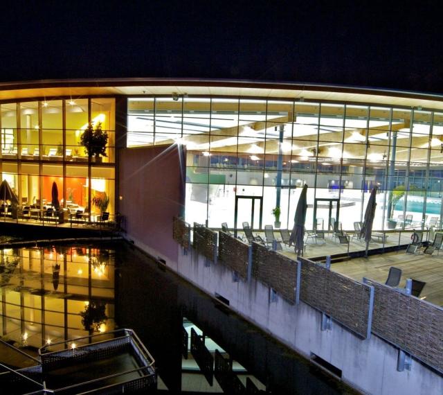 Teilansicht nachts auf das Hallenbad-Gebäude und den Liegebereich